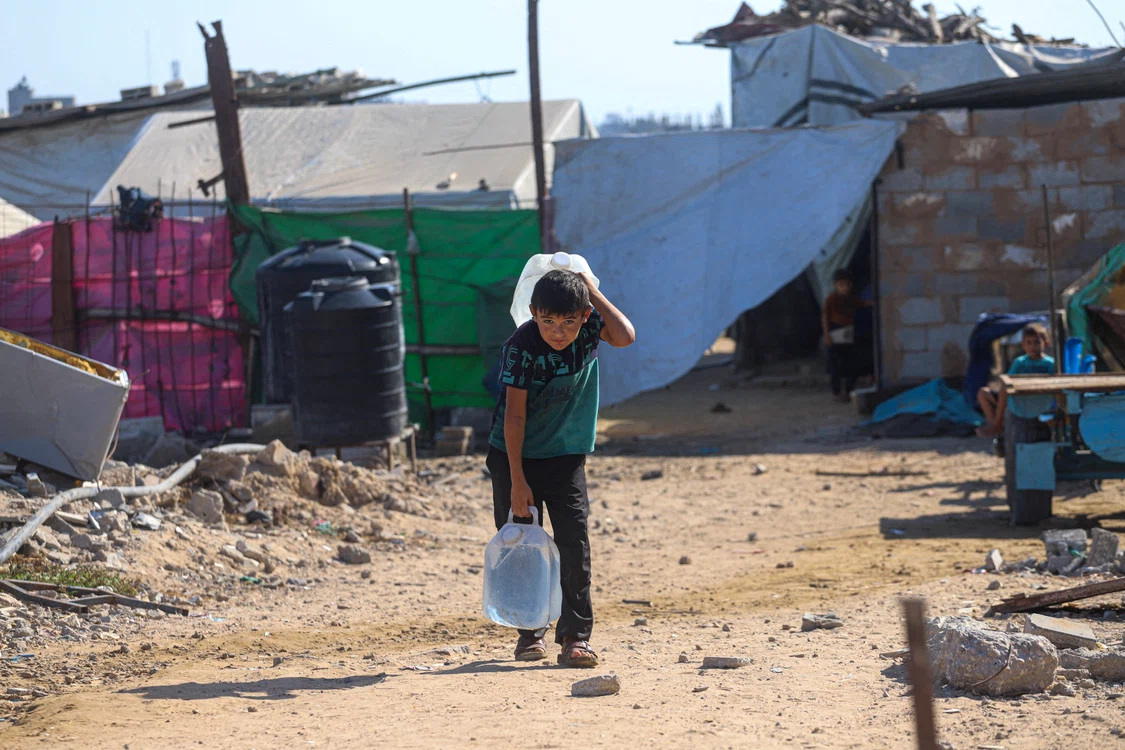Un copil palestinian cară bidoane cu apă într-o tabără din Gaza