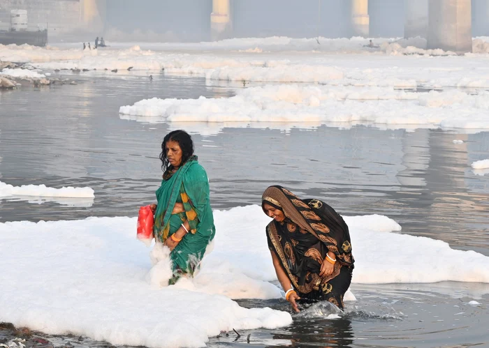 Două femei fac baie în râul Yamuna, plin cu o spumă toxică