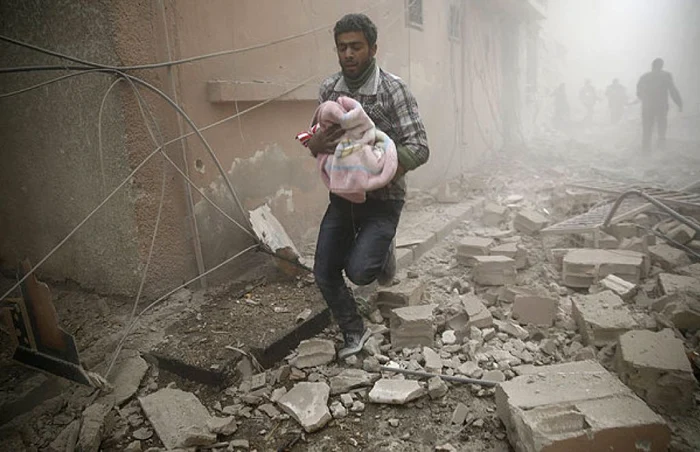 Un bărbat care un copil într-o pătură după o serie de bombardamente. FOTO AFP/ Getty Images