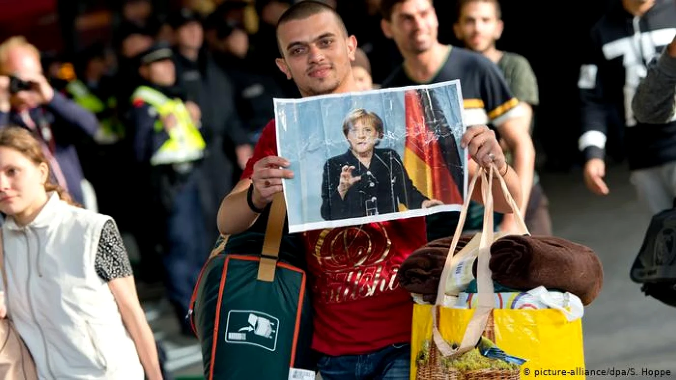 Refugiaţi care au sosit în 2015 la gara din München cu fotografii ale Angelei Merkel