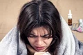 young woman is coughing while sitting home wrapped blanket jpg