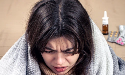 young woman is coughing while sitting home wrapped blanket jpg