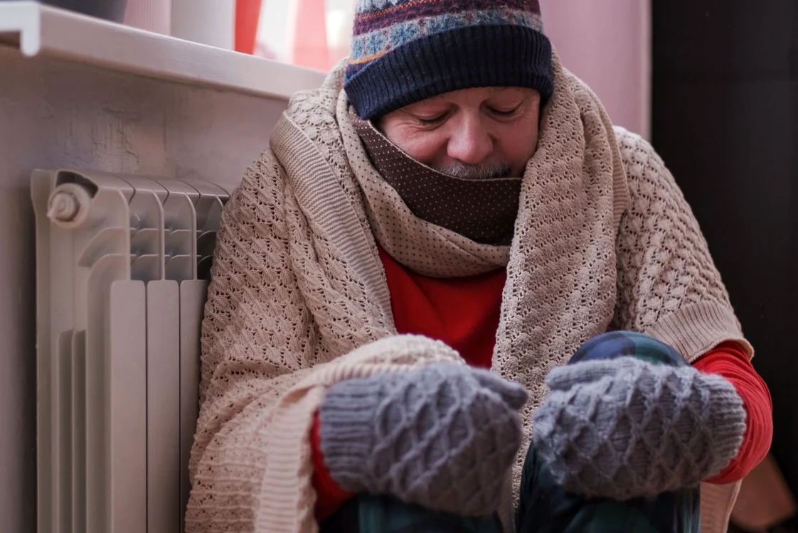 Foto bărbat îmbrăcat gros lipit de un calorifer 