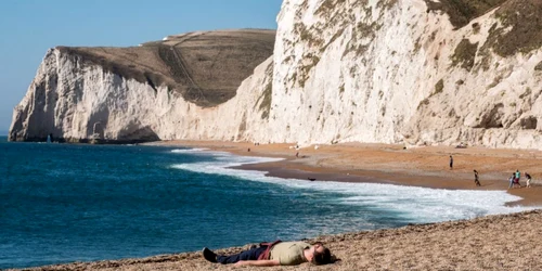 Un stă întins pe plajă la Durdle Door în timp ce oamenii se bucură de vremea excesiv de caldă în Dorset Marea Britanie FOTO Guliver / Getty Images / Matt Cardy