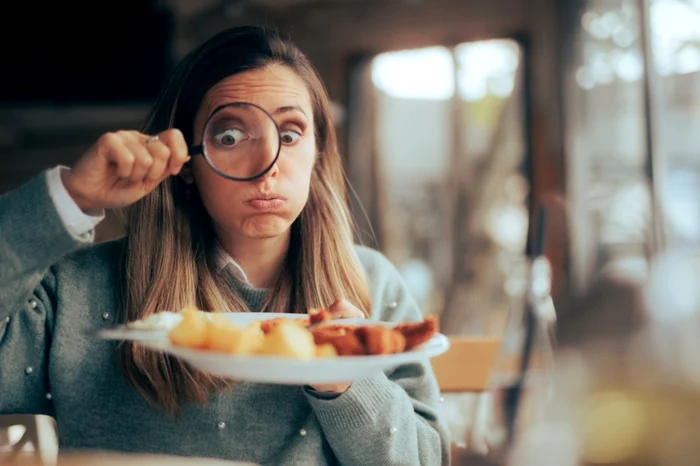 Femeie în restaurant, uitându-se la mâncarea din farfurie prin lupă