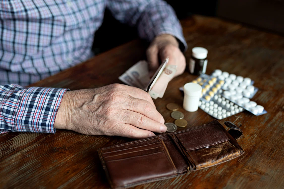 Un pensionar numără bănuții din portofel după ce a cumpărat medicamentele