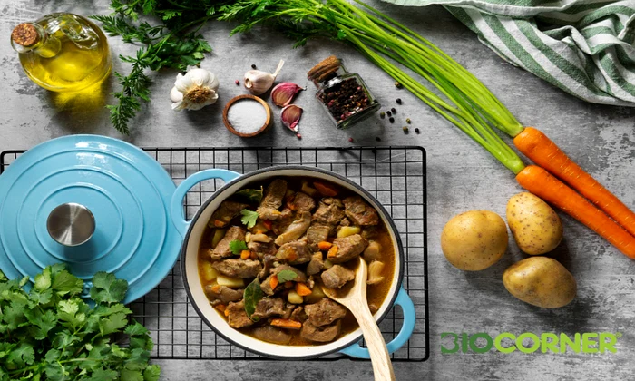tocanita de carne cu legume gatita intr o oala albastra inconjurata de ingrediente proaspete cartofi morcovi si usturoi biocorner png