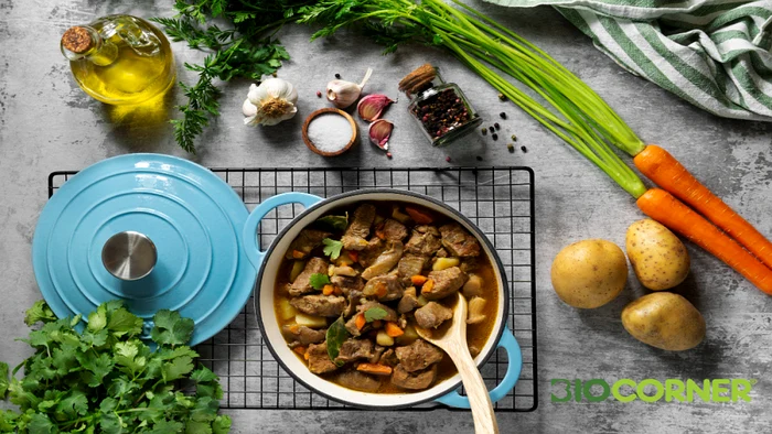 tocanita de carne cu legume gatita intr o oala albastra inconjurata de ingrediente proaspete cartofi morcovi si usturoi biocorner png