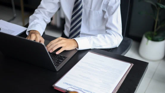 Avocat care lucrează în birou investighează cazul citind documente, folosind laptop-ul și tableta