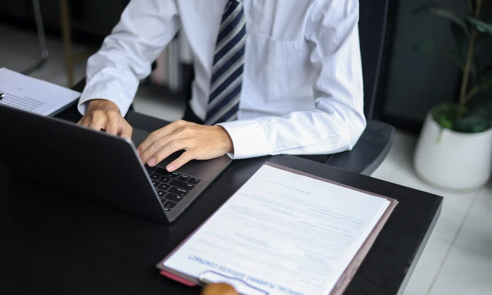 Avocat care lucrează în birou investighează cazul citind documente, folosind laptop-ul și tableta