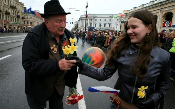 Bătrânul primește flori de la o tânără care venise să urmărească parada