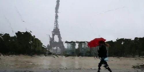 Picăturile de ploaie cazute pe geamul unei maşini deformeaza peisajul turnul Eiffel si silueta unei femei care se adăposteşte sub o umbrelă roşie în Paris FOTO Reuters