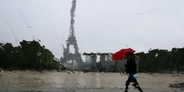 Picăturile de ploaie cazute pe geamul unei maşini deformeaza peisajul turnul Eiffel si silueta unei femei care se adăposteşte sub o umbrelă roşie în Paris FOTO Reuters