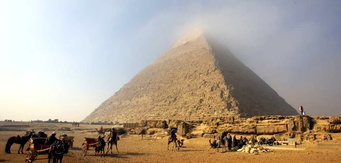 Oameni pe cămile aşteaptă turişti în timp ce un nor ceţos acoperă vârful Piramidei lui Cheops (Khufu) cea mai mare dintre cele trei piramide din Giza la periferia sudică a oraşului Cairo Egipt FOTO EPA – EFE / Khaled Elfiqi