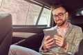 smiling successful stylish young businessman gray suit pink shirt using tablet riding back seat luxury car jpg