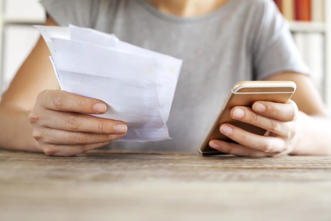 Cineva se uită la factura de telefon, ținând telefonul în mână