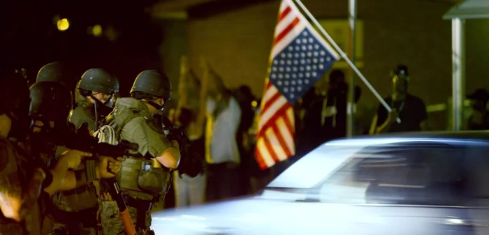 Care sunt americanii? Afroamericanii care flutură steagul SUA sau poliţiştii care ridică arma spre ei? FOTO Reuters