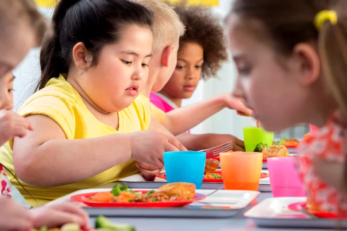 Mai mulți copii, inclusivi obezi care stau la masă și mănâncă Sursă foto Impact Monash Edu