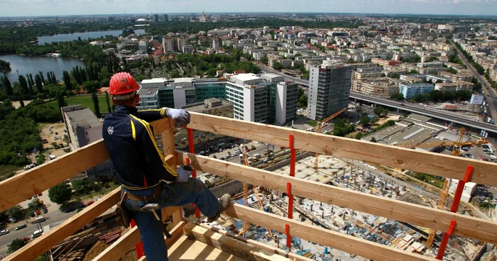 Un bărbat stă pe o terasă din lemn și privește un cartier plin de blocuri