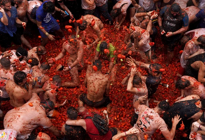 Oameni care se bat cu roși, în cadrul festivalului spaniol „Tomatina”. August 2023