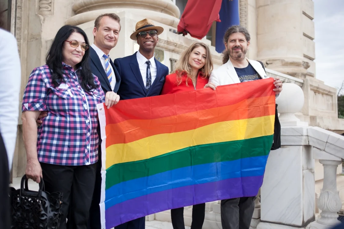 Adrian Coman şi Clabourn Hamilton, alături de părinţii românului şi alţi
 susţinători, afişează steagul în culorile curcubeului, simbolul 
comunităţii LGBT, în faţa sediului CCR FOTO Larisa Baltă
