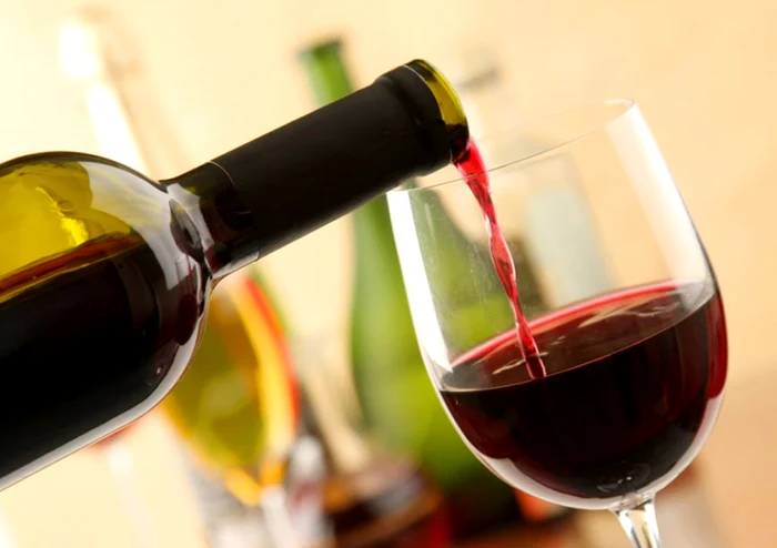 Cineva toarnă vin roșu din sticlă în pahar