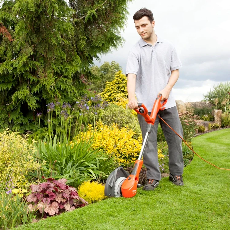 Bărbat tăind iarba cu coasa cu fir pentru delimita gazonul de flori Foto Gardening Naturally