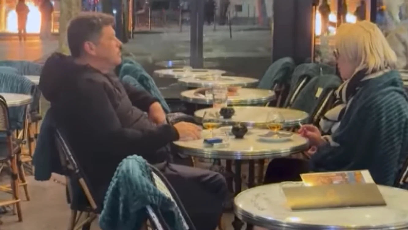 Un cuplu stă la un pahar lângă Arcul de Triumf, în timp ce orașul este în flăcări.