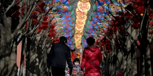 Un cuplu ţine un copil în picioare pe un scuter în timp ce trec pe sub decoraţiuni colorate pentru un târg înainte de Anul Nou Chinezesc în parcul Ditan de la Beijing China FOTO AP