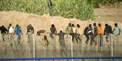 Emigranţi africani urca un gard de frontieră în timpul unei  încercări de a intra pe teritoriul spaniol în enclava Melilla FOTO Reuters