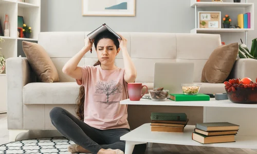 unpleased with closed eyes young girl covered head with notebook sitting floor coffee table living room jpg