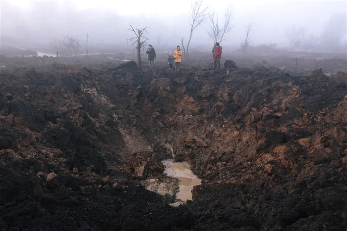 Localnici lângă craterul lăsat de o racheta rusească lângă Harkov. Foto: EPA-EFE