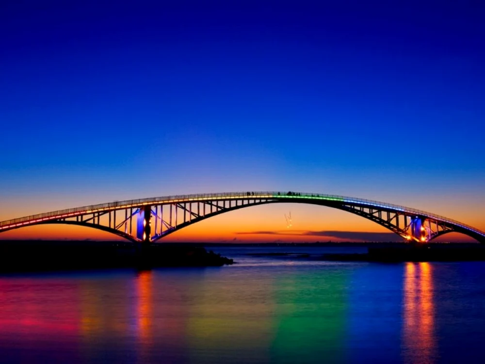 Arcul neon al acestui pod pietonal se reflectă în lagună, creând un arc dublu de o culoare intensă.