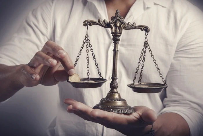 Un bărbat ține în palmă o balanță cu două talere și pune un ban într-unul dintre ele