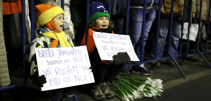 Doi copii ţin în mâini pancarte cu mesaje pentru jandarmi, lângă un buchet de flori, în Piaţa Victoriei FOTO INQUAM PHOTOS