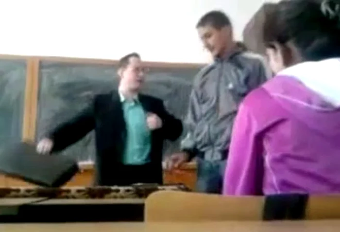 Profesorul aşteaptă ca elevul să se ridice de pe scaunul său pentru a-şi ocupa locul la catedră.