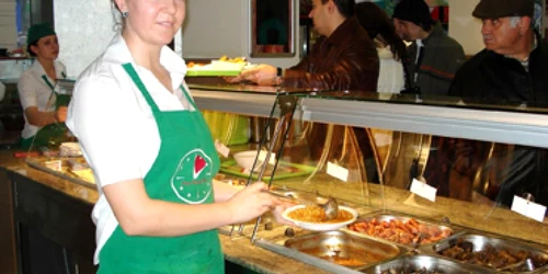 Angajata restaurantului umple o farfurie cu mâncare de fasole