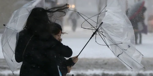 O femeie se luptă cu vântul puternic după ce umbrela i-a fost avariată