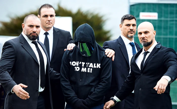 Concurenții poartă hanorace pe care scrie „Nu vorbi cu mine!” și sunt escortați de bodyguarzi