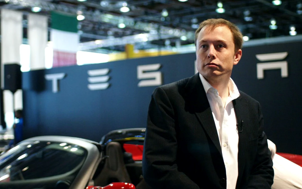 Elon Musk lângă sigla Tesla dintr-un showroom