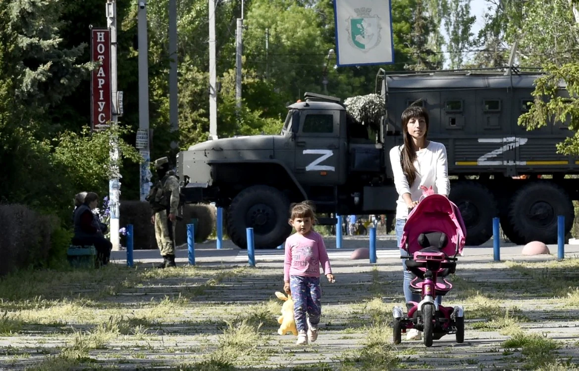 20 mai 2022 - o femeie şi un copil se plimbă într-un parc în timp ce un soldat rus patrulează pe străzile din  Skadovsk regiunea Herson FOTO AFP 