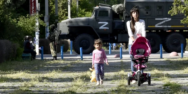 20 mai 2022 - o femeie şi un copil se plimbă într-un parc în timp ce un soldat rus patrulează pe străzile din  Skadovsk regiunea Herson FOTO AFP 