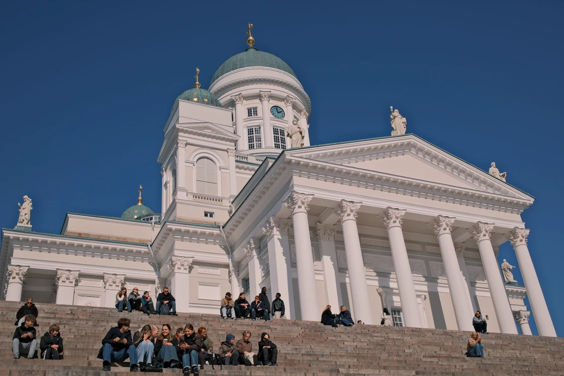 Oameni relaxându-se pe treptele Catedralei din Helsinki sub un cer albastru senin.