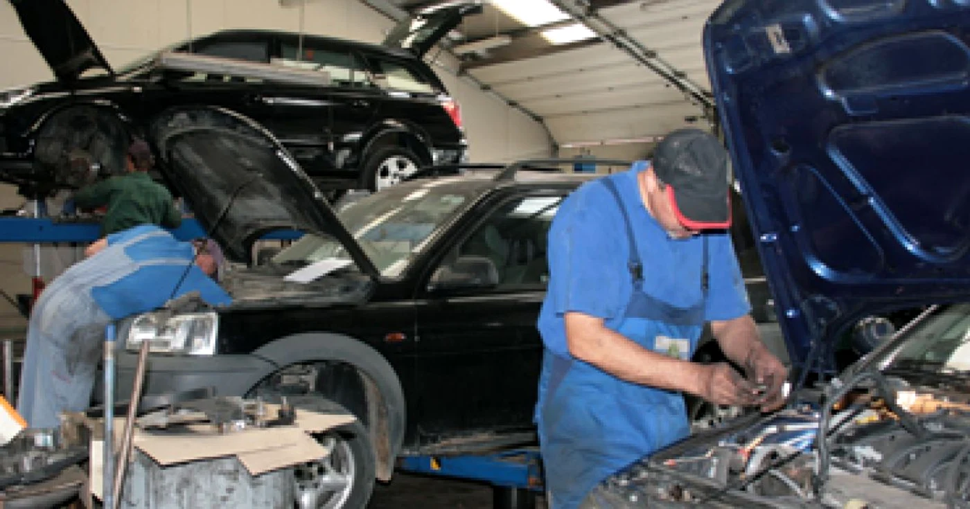 Doi mecanci repară mașini într-un service auto
