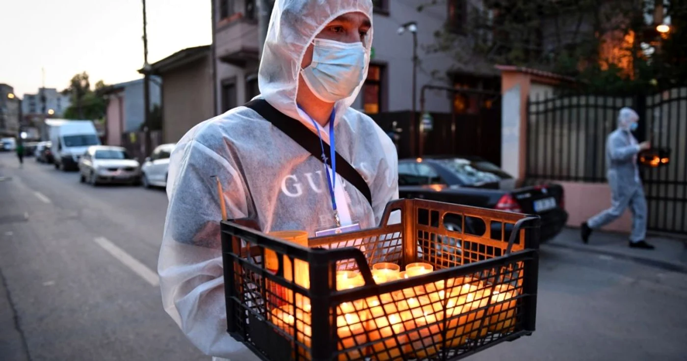 Voluntar împărţind lumină de Paşti în contextul pandemiei de coronavirus FOTO AFP/ Daniel Mihăilescu