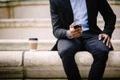 un barbat in costum sta cu un telefon iPhone 17 in mana si cu o cafea alaturi jpg