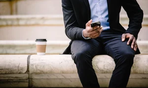 un barbat in costum sta cu un telefon iPhone 17 in mana si cu o cafea alaturi jpg