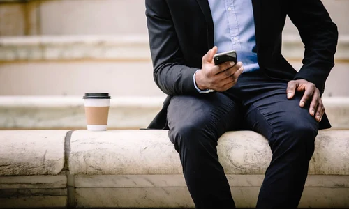 un barbat in costum sta cu un telefon iPhone 17 in mana si cu o cafea alaturi jpg