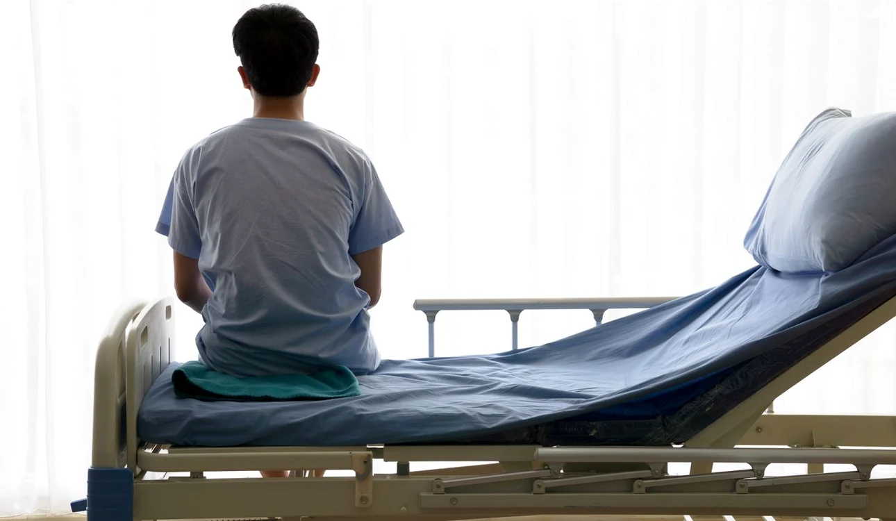 Un bărbat se uită pe geam în timp ce stă pe un pat de spital