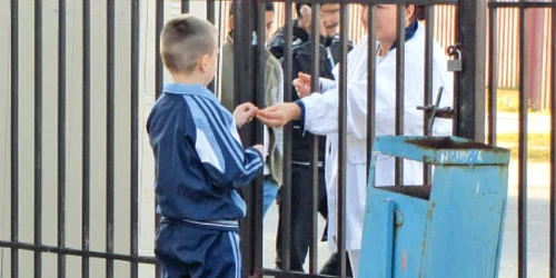 Părinţii le dau pacheţelele copiilor prin grilajul de fier de la intrare